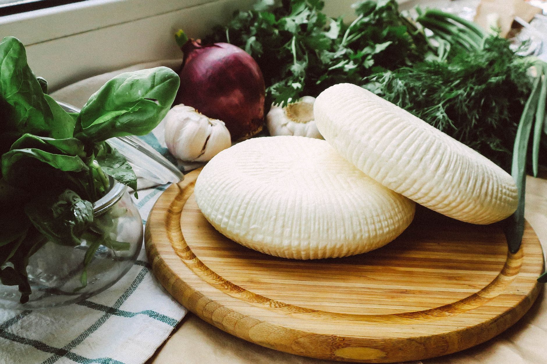Deux fromages frais moulés sur une planche en bois, entourés de basilic, d'oignon rouge et d'ail