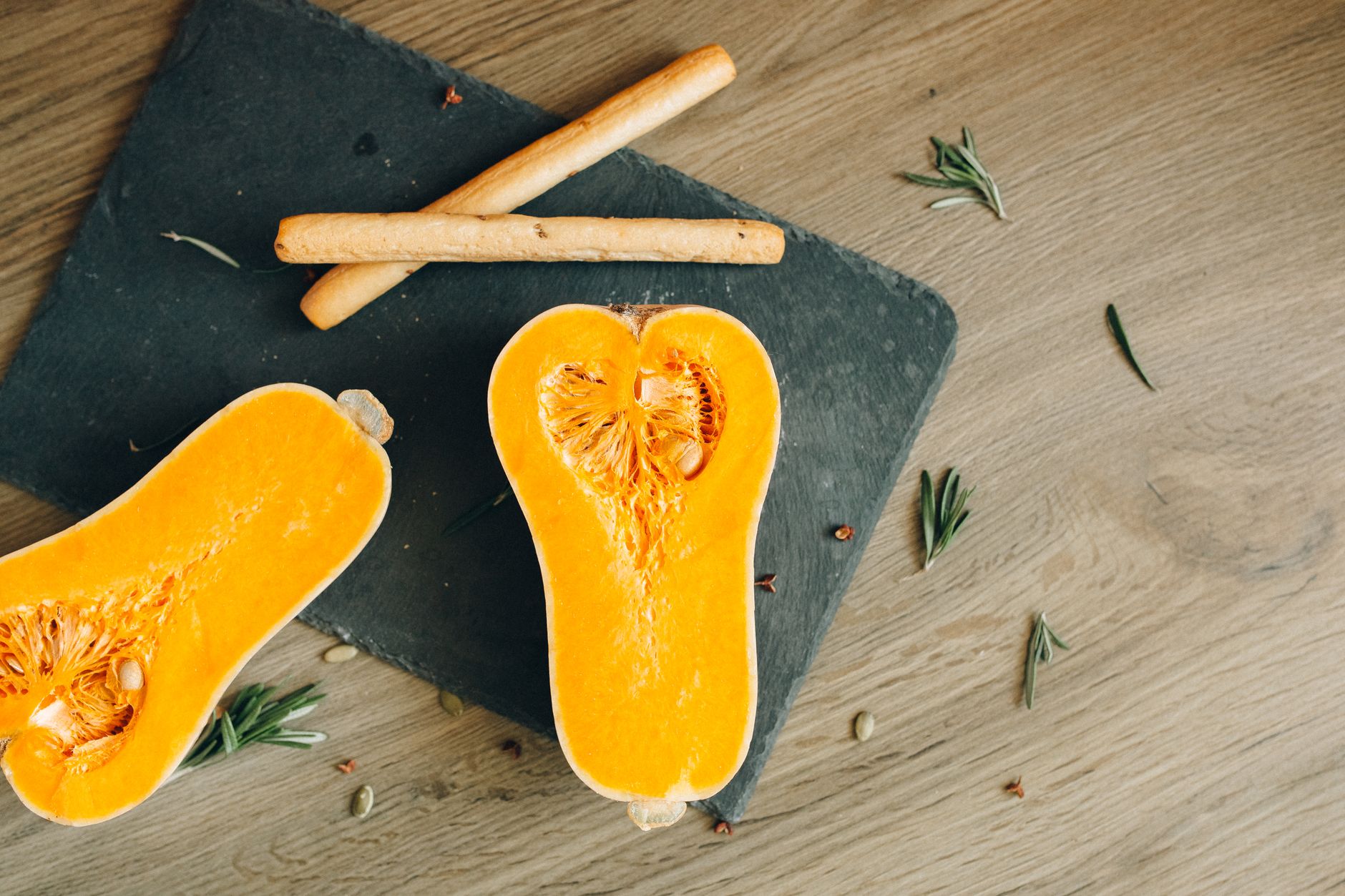 Deux moitiés de courge butternut crue avec leurs graines, posées sur une planche en ardoise et une table en bois.