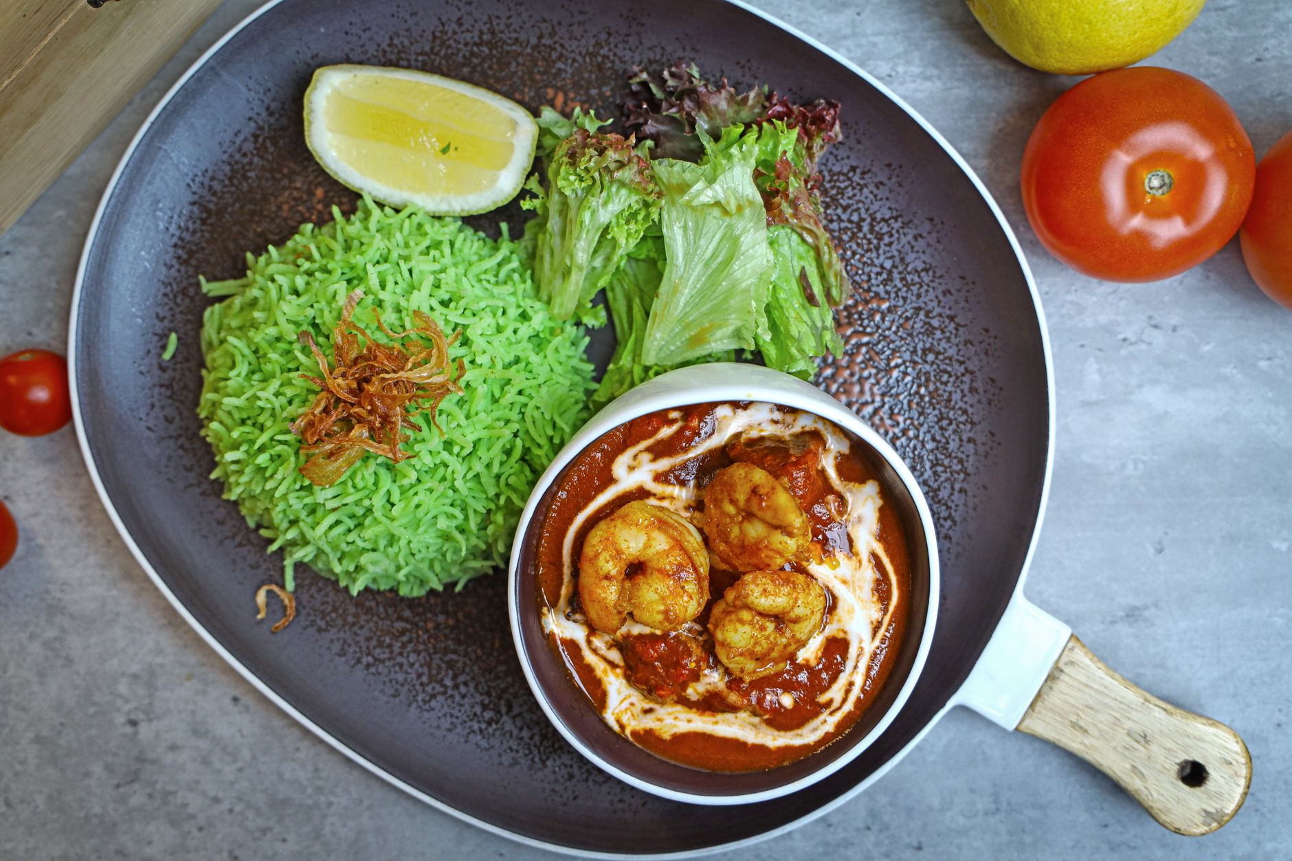 Plat de crevettes en sauce rouge et crème, servi avec du riz vert, de la salade et un quartier de citron.
